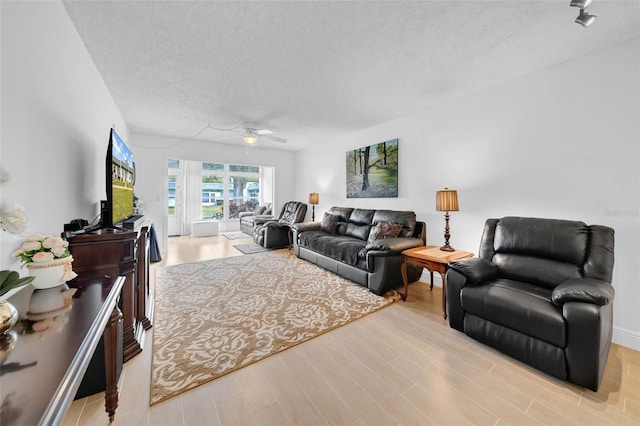 living room featuring ceiling fan, a textured ceiling, and light wood-type flooring