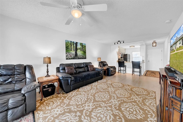 living room featuring ceiling fan, a textured ceiling, and light wood-type flooring