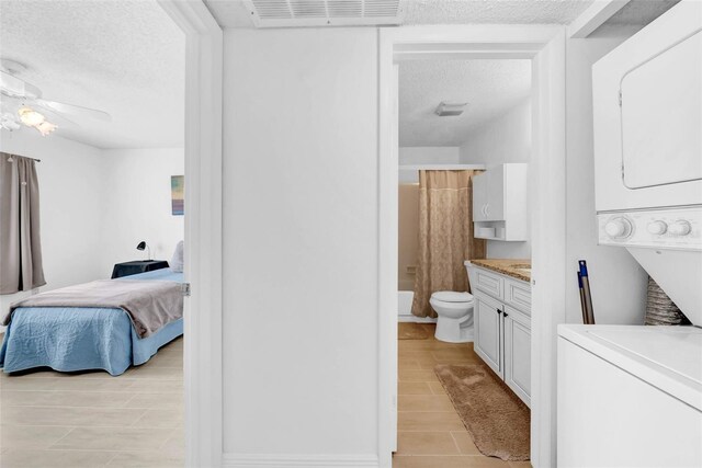 bathroom featuring ceiling fan, stacked washer and clothes dryer, vanity, a textured ceiling, and toilet