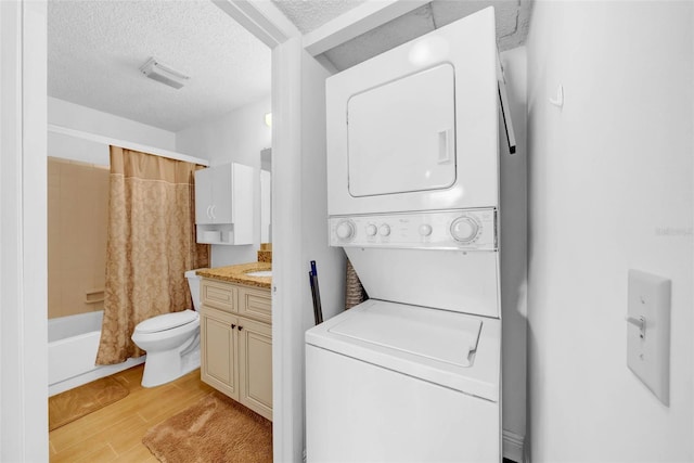 laundry room featuring stacked washer and dryer, a textured ceiling, and light hardwood / wood-style flooring