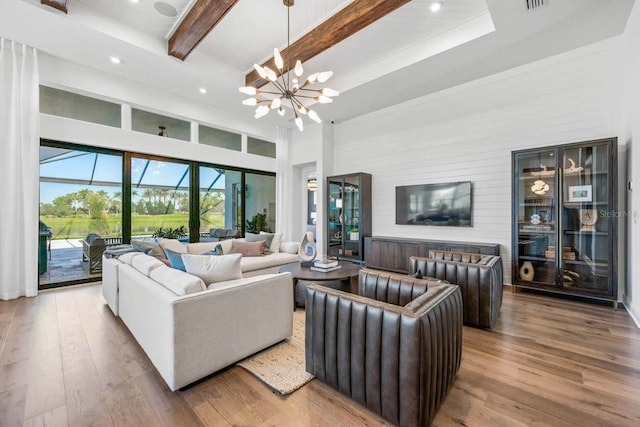 living room with beamed ceiling, a towering ceiling, a notable chandelier, and light hardwood / wood-style floors