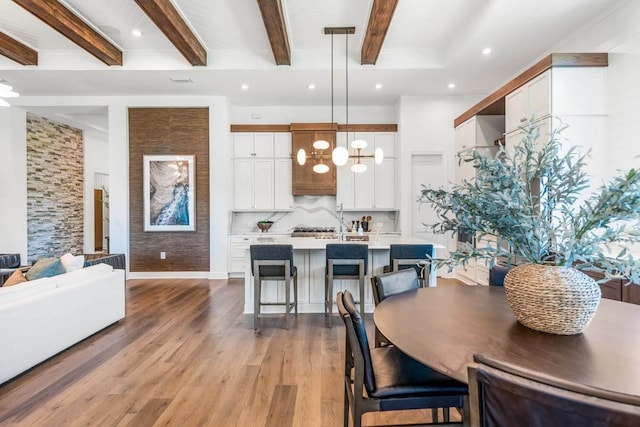 dining area featuring an inviting chandelier, beam ceiling, and light hardwood / wood-style floors