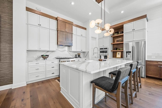 kitchen with appliances with stainless steel finishes, decorative light fixtures, white cabinetry, an island with sink, and light stone countertops