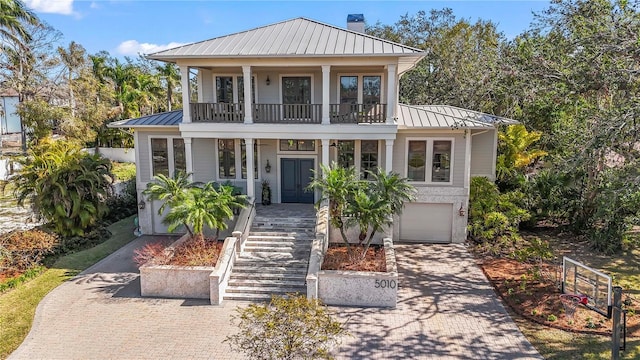 view of front of home with a balcony, a chimney, metal roof, a standing seam roof, and decorative driveway