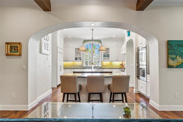 kitchen featuring a center island, hanging light fixtures, beam ceiling, hardwood / wood-style floors, and white cabinets