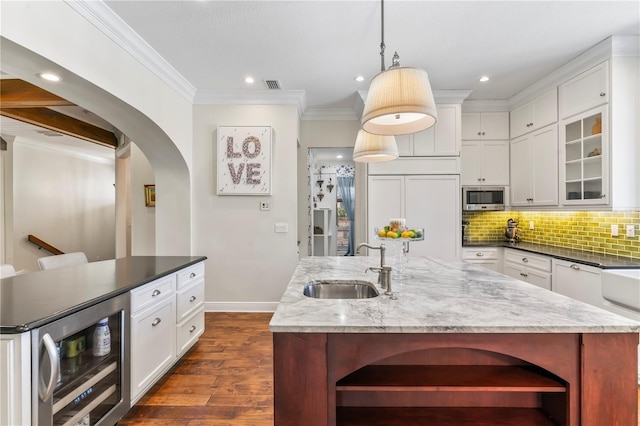 kitchen featuring tasteful backsplash, wine cooler, stainless steel microwave, a kitchen island with sink, and a sink