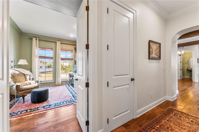 hall featuring ornamental molding, arched walkways, wood-type flooring, and baseboards