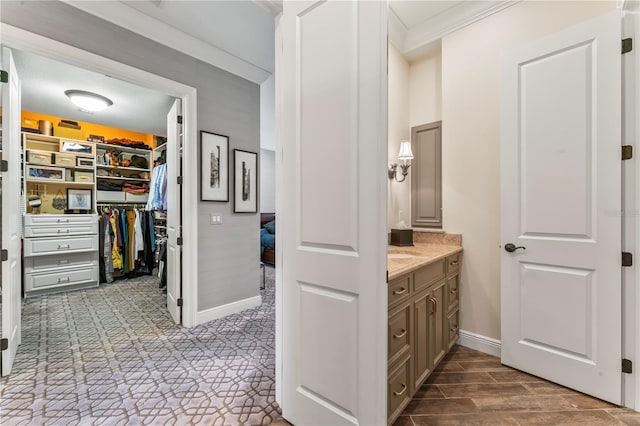 bathroom with baseboards, a walk in closet, crown molding, and vanity