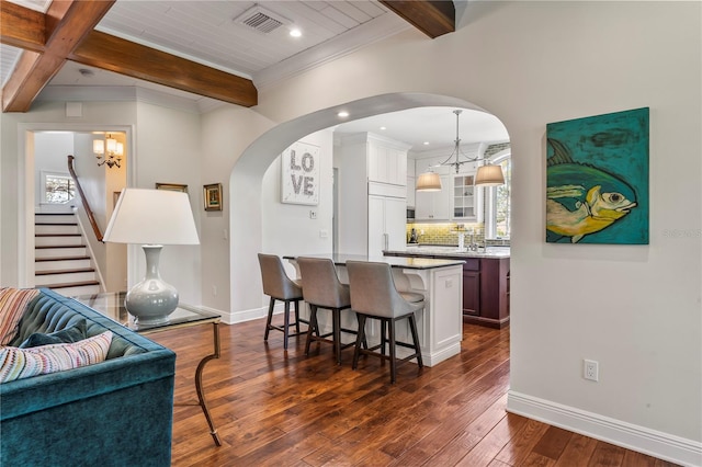 kitchen featuring a breakfast bar, dark wood-style flooring, visible vents, beam ceiling, and glass insert cabinets