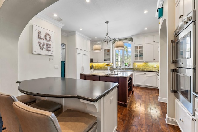 kitchen featuring dark wood-style floors, a center island with sink, visible vents, glass insert cabinets, and stainless steel double oven