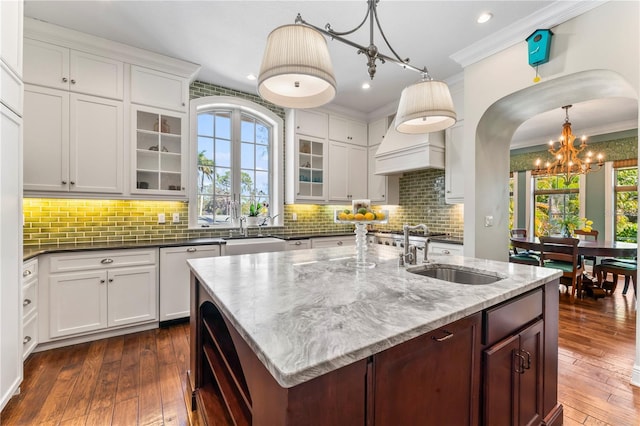 kitchen with ornamental molding, a kitchen island with sink, sink, and decorative light fixtures