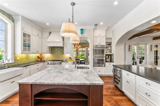 kitchen with arched walkways, custom range hood, wine cooler, stainless steel appliances, and open shelves