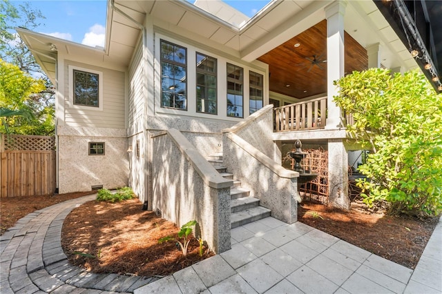 doorway to property featuring a porch, stucco siding, ceiling fan, and fence