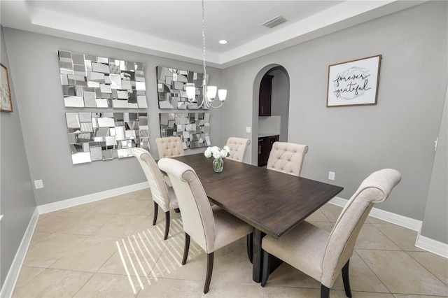 dining area featuring arched walkways, light tile patterned flooring, visible vents, baseboards, and a tray ceiling