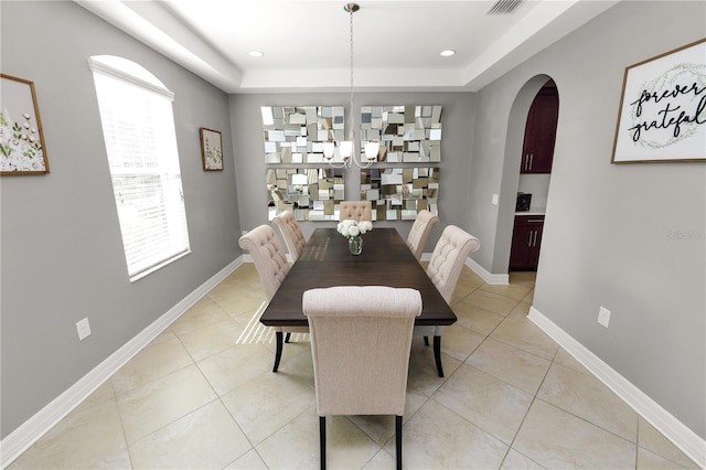 dining space with baseboards, a tray ceiling, arched walkways, and light tile patterned flooring