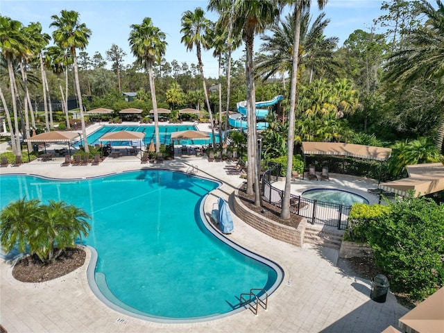 community pool with a patio area, a hot tub, and a water slide