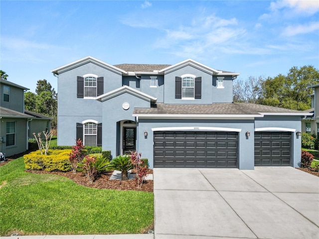 traditional-style home with stucco siding, a shingled roof, concrete driveway, an attached garage, and a front yard