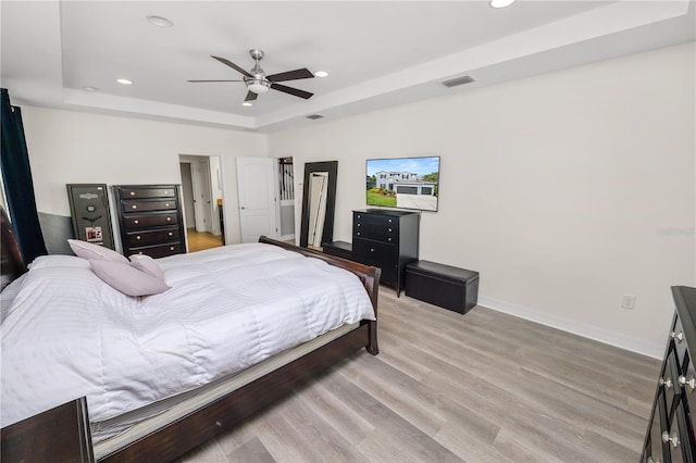 bedroom with a tray ceiling, recessed lighting, visible vents, light wood-style floors, and baseboards