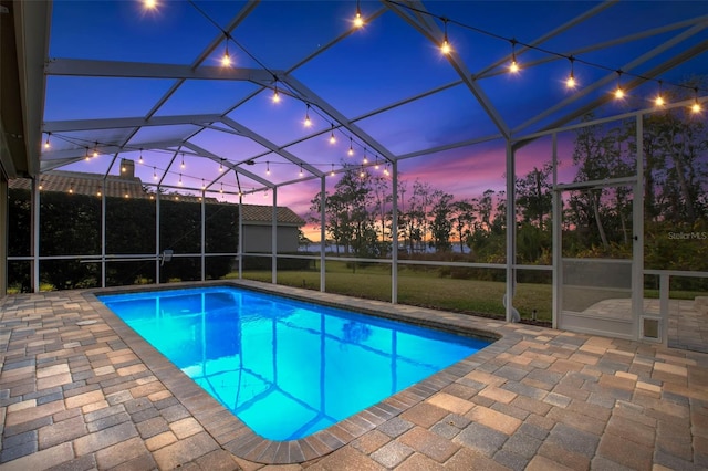 pool at dusk featuring a yard, a patio area, and glass enclosure