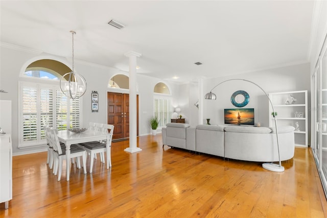 living room with an inviting chandelier, crown molding, light wood-type flooring, and ornate columns