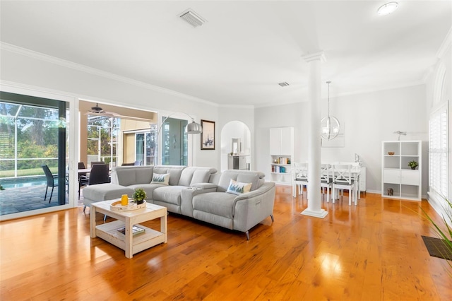 living room with crown molding, ornate columns, ceiling fan with notable chandelier, and light wood-type flooring