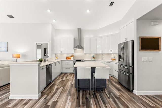 kitchen with white cabinetry, wall chimney range hood, kitchen peninsula, and appliances with stainless steel finishes