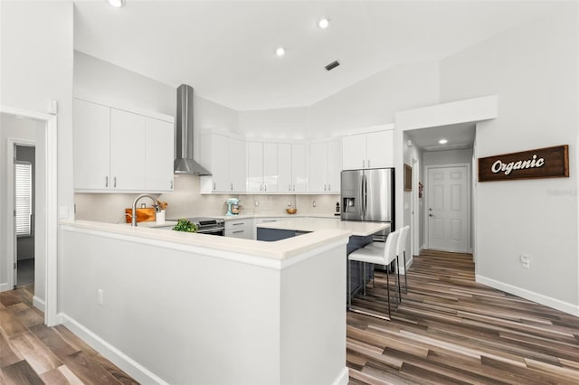 kitchen featuring white cabinetry, backsplash, kitchen peninsula, stainless steel appliances, and wall chimney exhaust hood