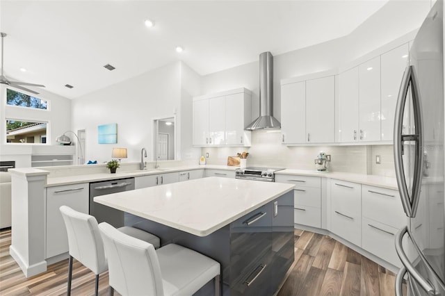 kitchen with wall chimney exhaust hood, stainless steel appliances, a center island, and white cabinets