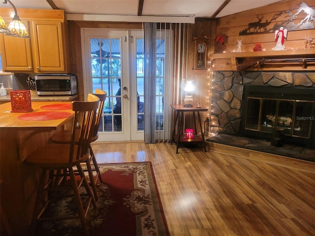 dining room featuring french doors, a stone fireplace, hardwood / wood-style floors, and wood walls