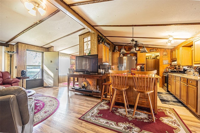 dining space featuring wood walls, lofted ceiling with beams, ceiling fan, light hardwood / wood-style floors, and a textured ceiling