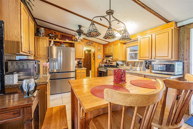 kitchen with pendant lighting, light tile patterned floors, vaulted ceiling with beams, stainless steel appliances, and a textured ceiling