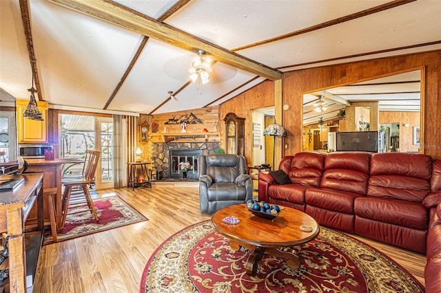 living room featuring vaulted ceiling with beams, wooden walls, ceiling fan, a fireplace, and light hardwood / wood-style floors