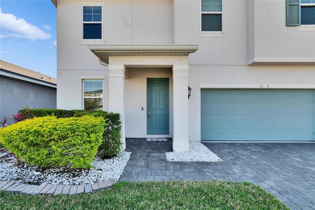 doorway to property featuring an attached garage, decorative driveway, and stucco siding