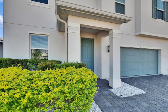 doorway to property featuring decorative driveway, an attached garage, and stucco siding