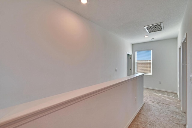 hallway featuring a textured ceiling, recessed lighting, light colored carpet, visible vents, and baseboards