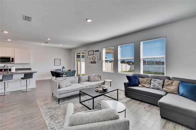 living area featuring light wood finished floors, visible vents, a textured ceiling, and recessed lighting