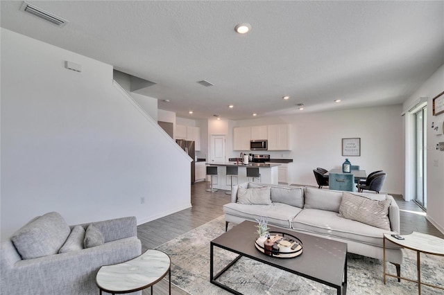 living area featuring light wood-style floors, recessed lighting, visible vents, and a textured ceiling