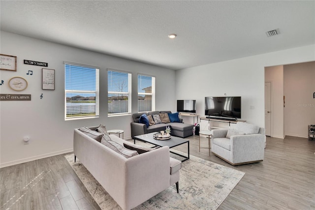 living room with visible vents, a textured ceiling, baseboards, and wood finished floors