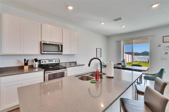 kitchen featuring a sink, visible vents, white cabinetry, appliances with stainless steel finishes, and a center island with sink