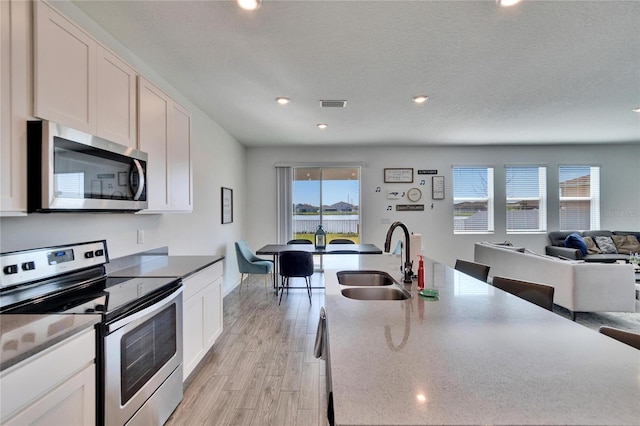 kitchen featuring visible vents, open floor plan, stainless steel appliances, light wood-type flooring, and a sink