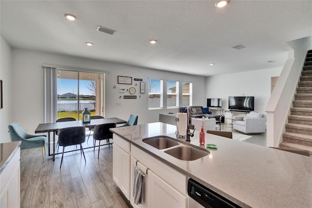 kitchen with visible vents, a sink, light wood-type flooring, white cabinetry, and stainless steel dishwasher