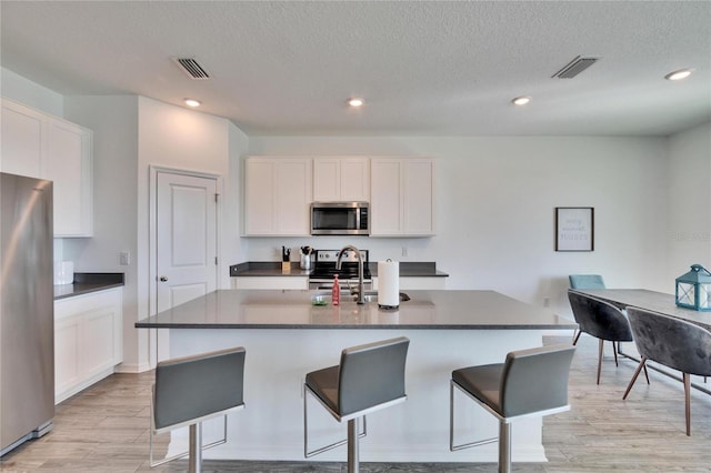 kitchen with dark countertops, a breakfast bar, visible vents, and stainless steel appliances