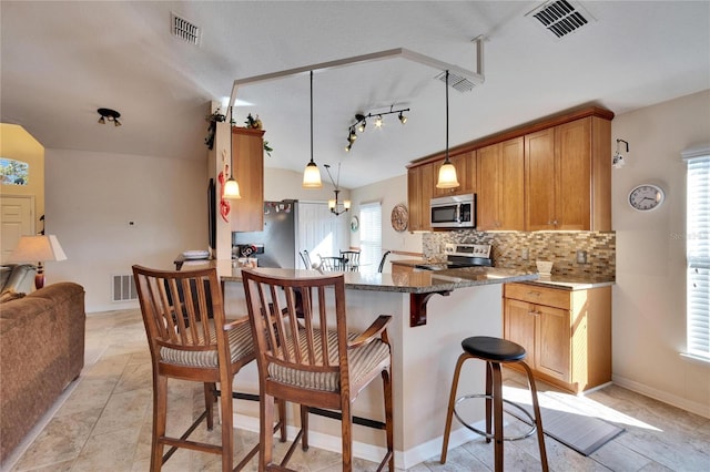 kitchen featuring vaulted ceiling, decorative light fixtures, tasteful backsplash, kitchen peninsula, and stainless steel appliances