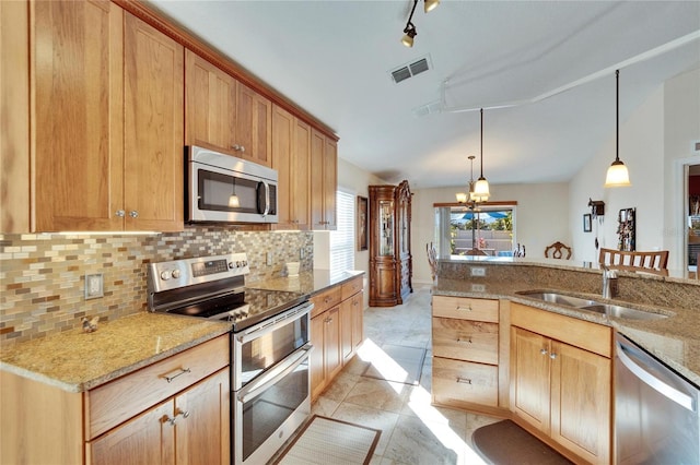 kitchen with decorative light fixtures, sink, backsplash, stainless steel appliances, and light stone countertops