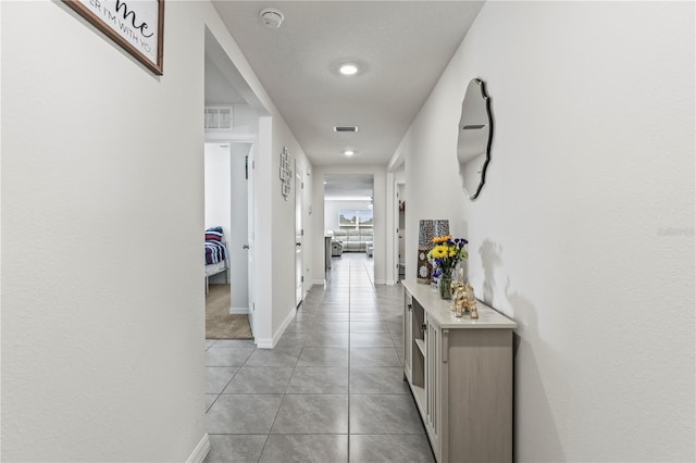 hall with light tile patterned floors, baseboards, and visible vents