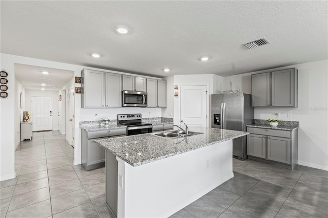 kitchen with a center island with sink, gray cabinets, visible vents, appliances with stainless steel finishes, and a sink