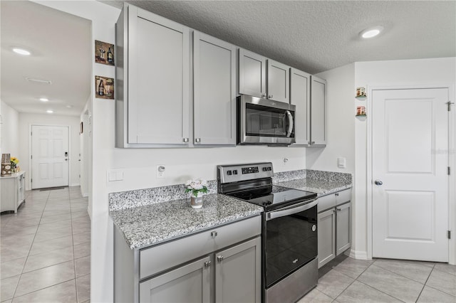 kitchen featuring a textured ceiling, light tile patterned flooring, gray cabinetry, stainless steel appliances, and light stone countertops