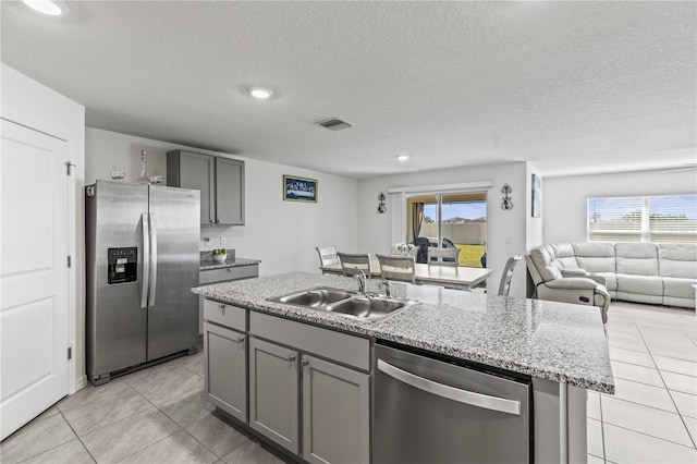 kitchen with gray cabinets, visible vents, appliances with stainless steel finishes, a kitchen island with sink, and a sink