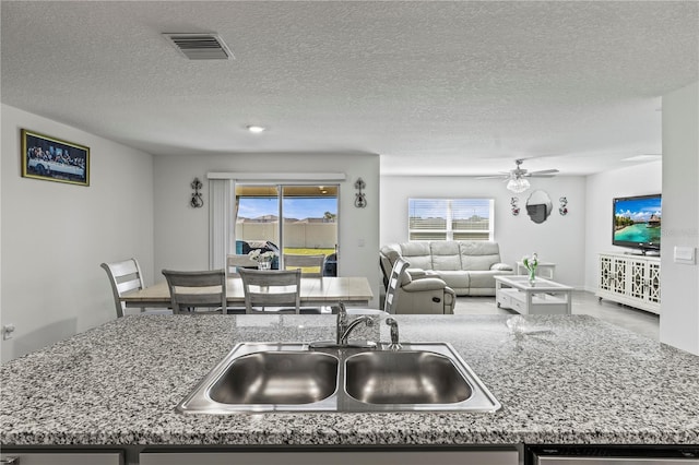 kitchen featuring open floor plan, light stone counters, a sink, and visible vents