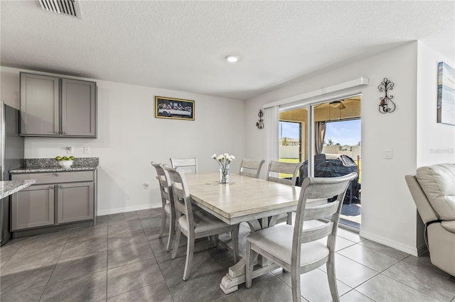 dining space with a textured ceiling, dark tile patterned floors, visible vents, and baseboards